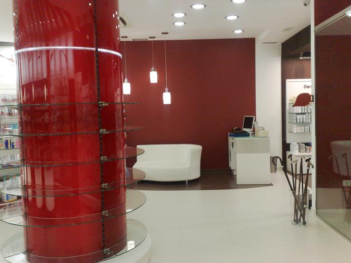 Columna roja con repisas transparentes en interior de farmacia, paredes rojas y diseño limpio y blanco