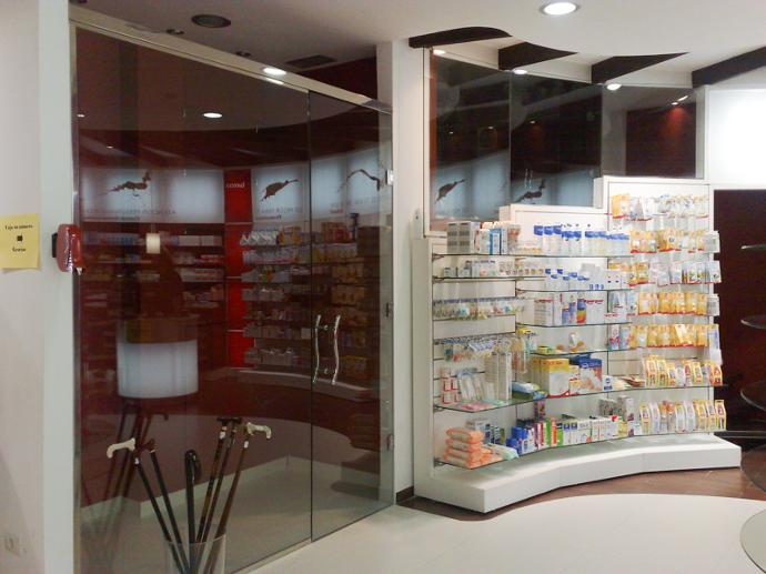 Interior de farmacia con tonos rojos y mobiliario blanco, entrada transparente